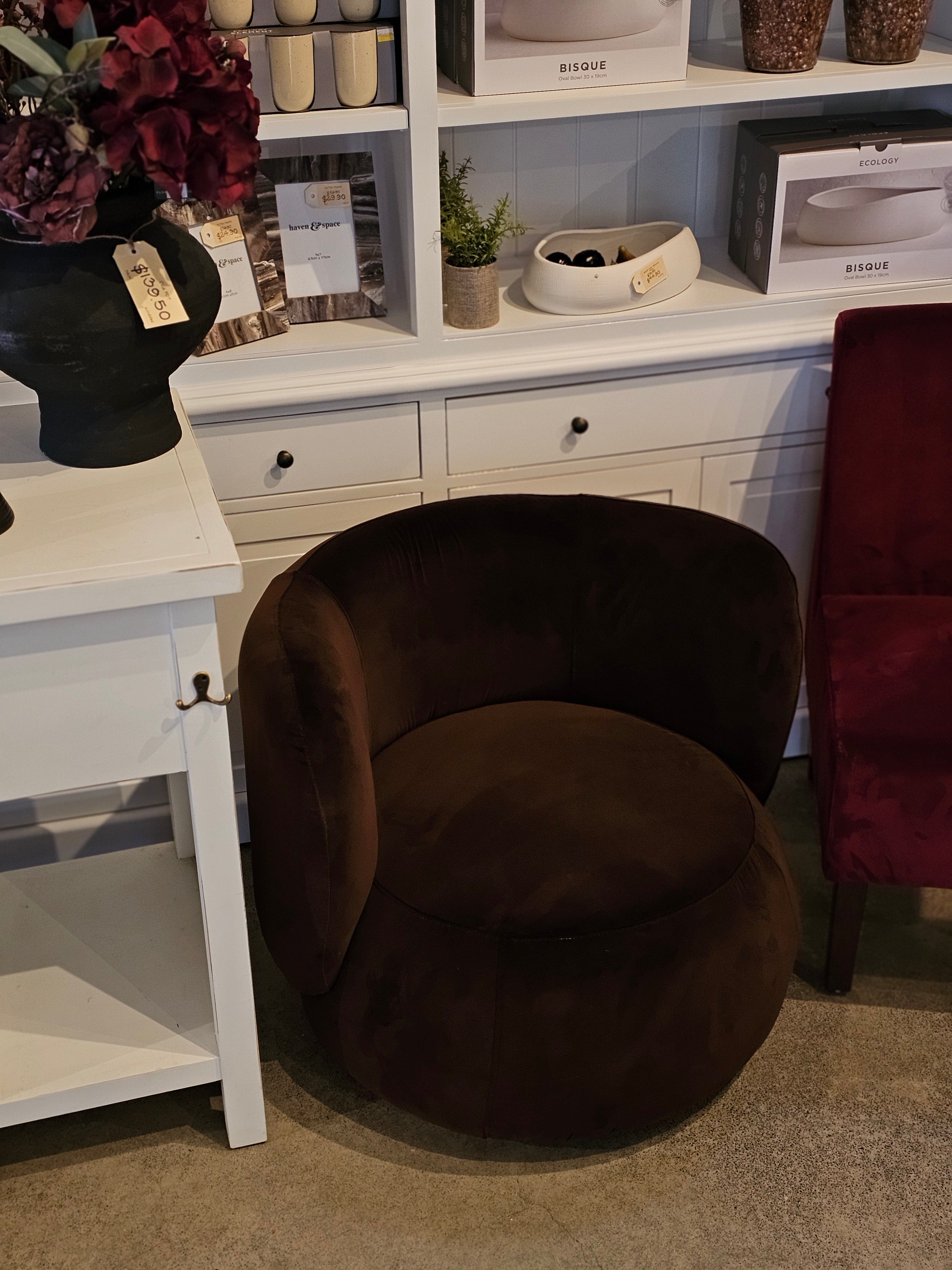 Mila Swivel Armchair in rich brown velvet with curved backrest, displayed in a modern showroom setting for contemporary interiors.